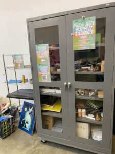 Large gray cabinet with glass doors filled with art supplies.