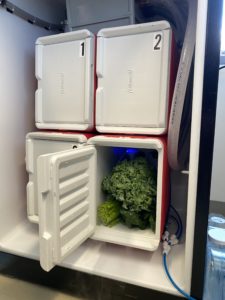 Open fridge displaying four inner coolers. One of them is open with leafy greens inside. 