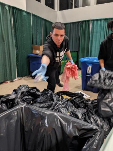 A volunteer properly disposing of trash in the trash bin during the waste audit at Green Game 2023. Photo by Ben Auger/George Mason University